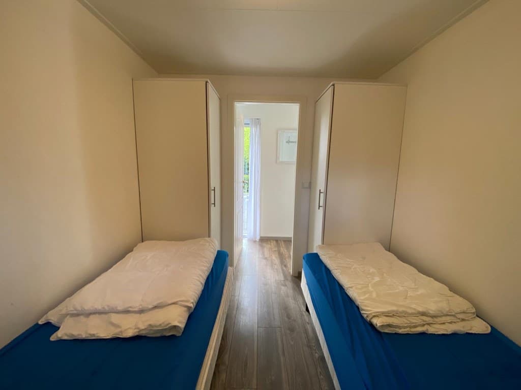 Slaapkamer met twee eenpersoonsbedden, kasten en toegang tot een gang met natuurlijk licht.