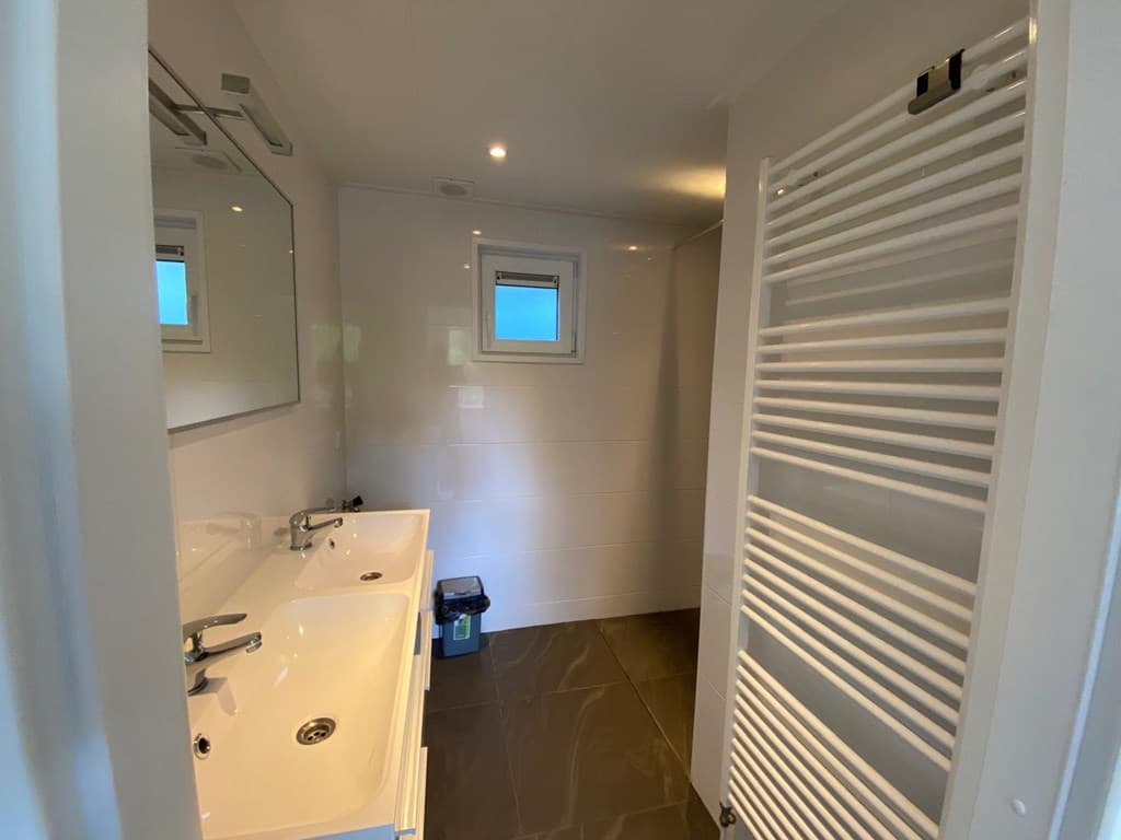 Moderne badkamer met dubbele wastafel, grote spiegel en handdoekenradiator, lichte tegels en raam voor natuurlijk licht