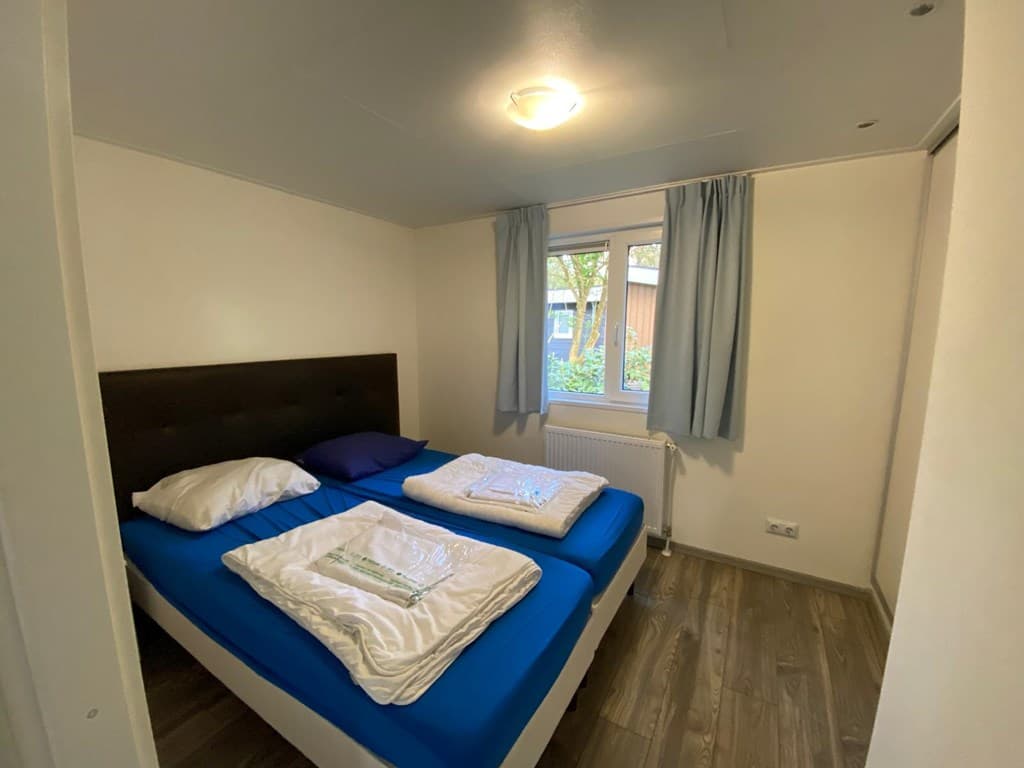 Slaapkamer met een tweepersoonsbed, witte beddengoed en een raam met uitzicht op groen buiten.