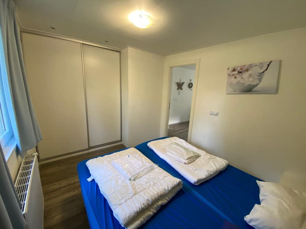 Slaapkamer met twee bedden, kledingkast en verwarming, lichte wanden en vloerbedekking in warme tinten.