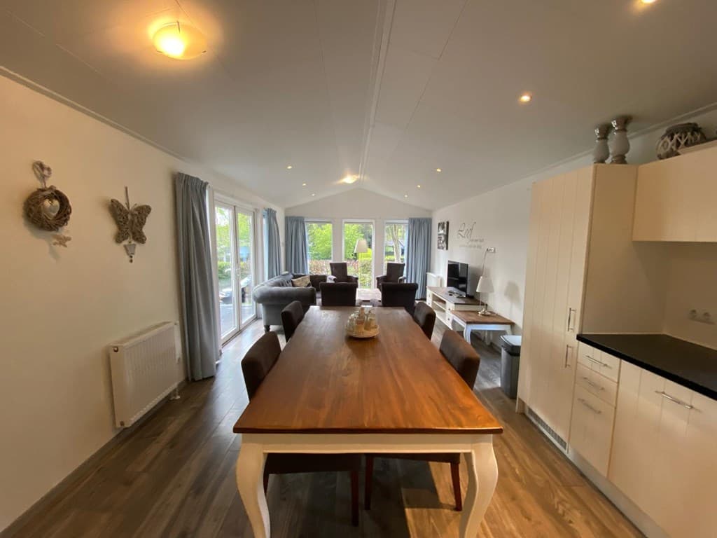 Eethoek met lange houten tafel en stoelen, open woonkamer met banken en grote ramen naar buiten.