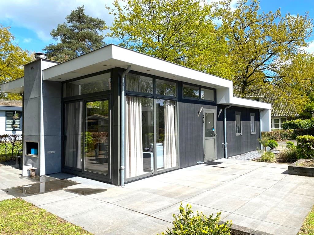 Moderne vakantiewoning met grote ramen en patio, omringd door groen en bomen in EuroParcs De Achterhoek.