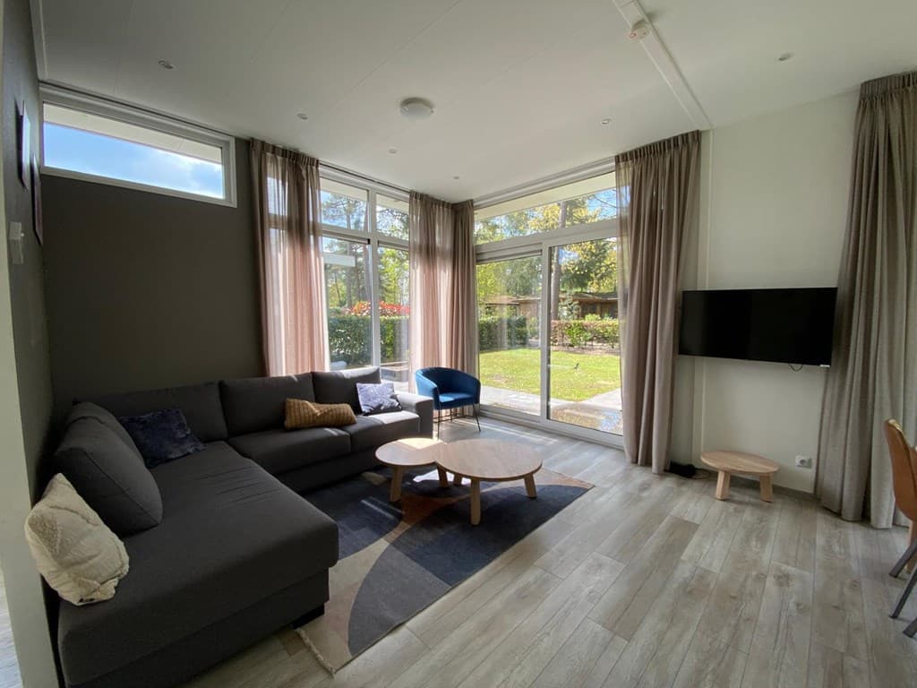 Modern interieur met een zithoek, grote ramen en toegang tot de tuin bij EuroParcs De Achterhoek in Lochem