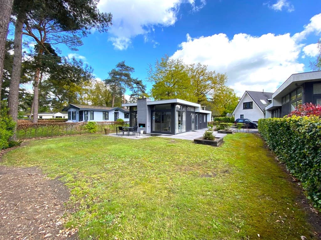 Moderne vakantiewoning met een ruim grasveld en terras, omgeven door bomen en andere woningen in EuroParcs De Achterhoek.
