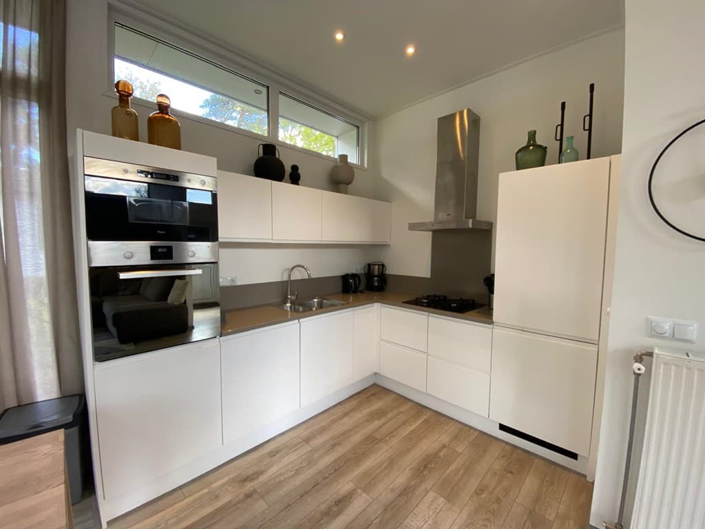 Moderne keuken met witte kastjes, inbouwapparatuur en houten vloer, lichtinval door raampjes bovenaan