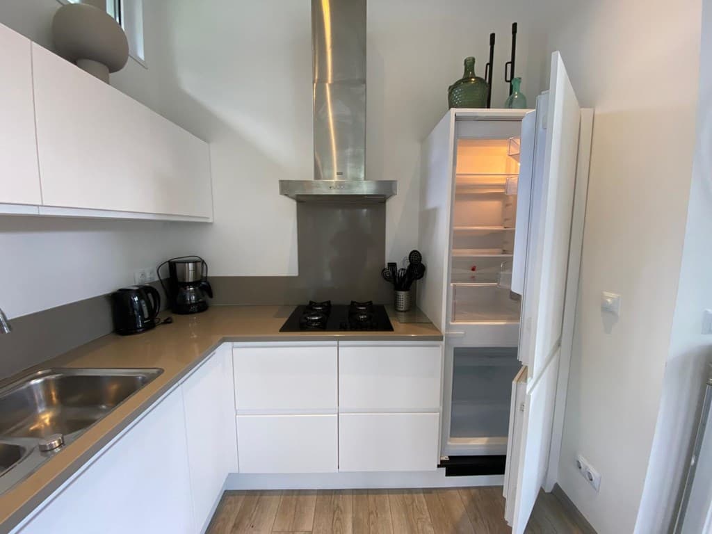 Keuken met moderne inrichting, gasfornuis, koelkast met een open deur en een gootsteen zichtbaar in lichte tinten.