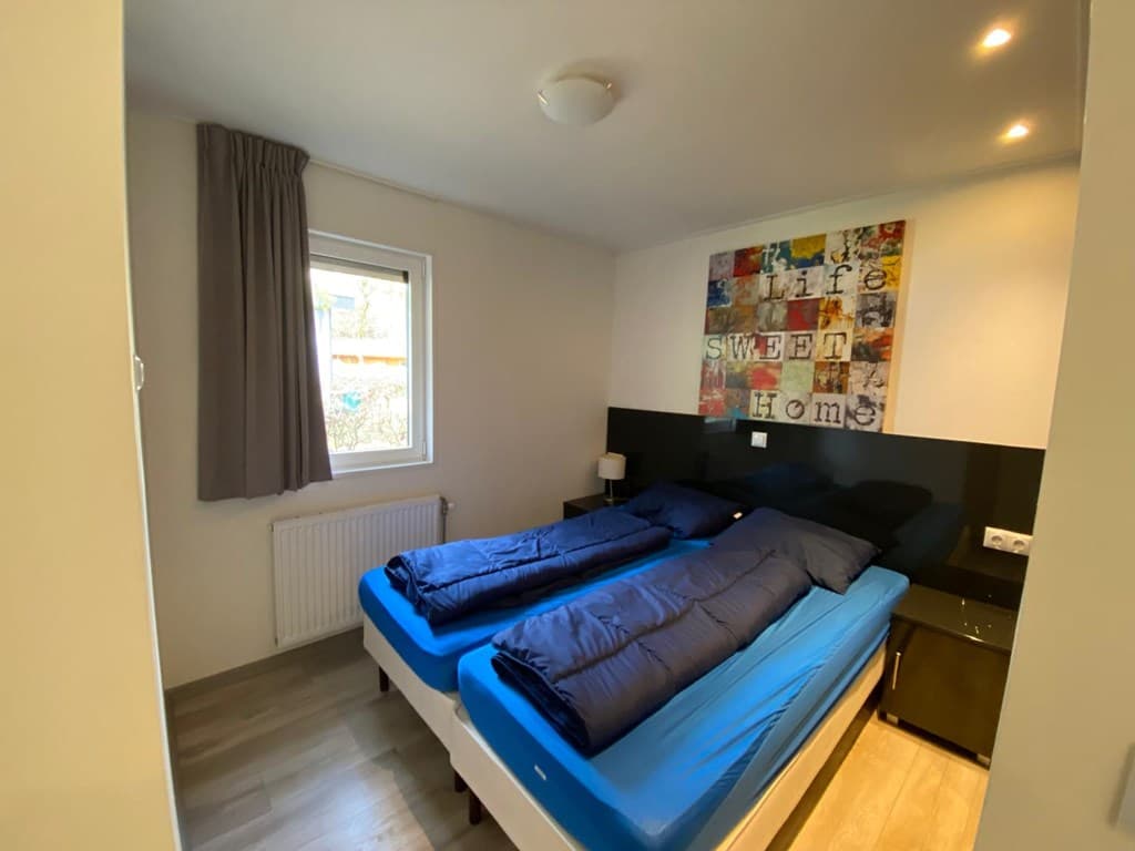 Slaapkamer met twee losse eenpersoonsbedden, raam, moderne wanddecoratie en nachtkastje.