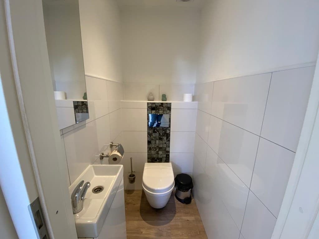 Wit betegeld toilet met wastafel en moderne sanitaire voorzieningen in een compacte ruimte.