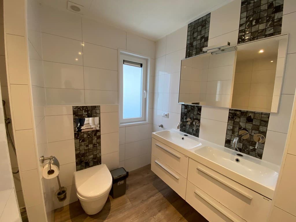 Moderne badkamer met dubbele wastafel, toilet en raam, betegeld met witte en donkere tegels