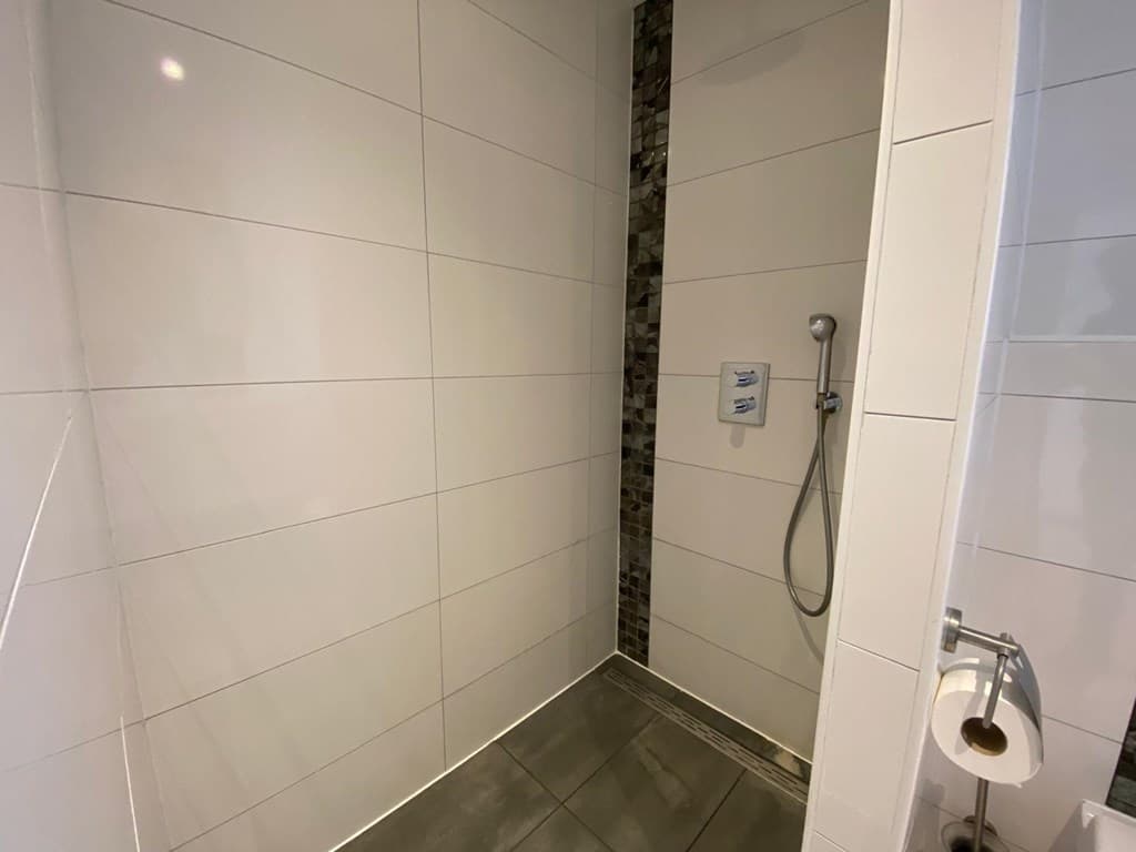 Nette inloopdouche met tegelwanden en een moderne douchekop, voorzien van een handdoekhouder en toiletrand.