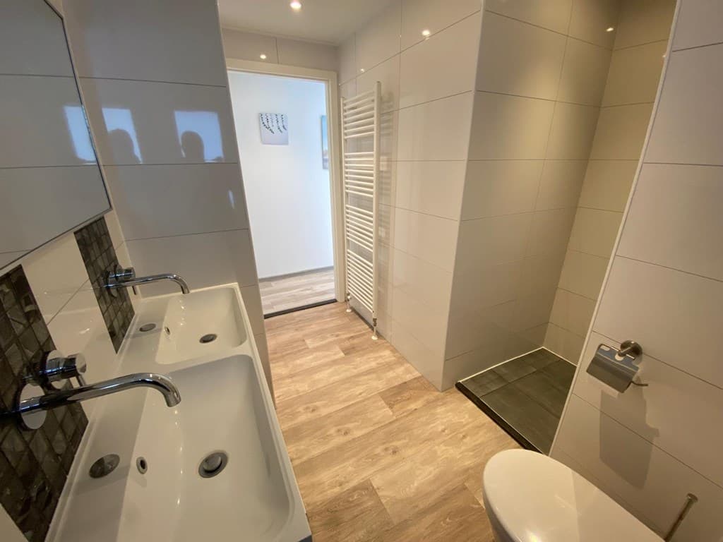 Moderne badkamer met dubbele wastafel, douche, toilet en lange wandverwarming. Licht en strak ingericht.