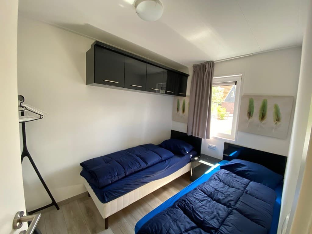 Slaapkamer met twee bedden, wandkast boven de bedden en een raam met uitzicht op buiten.
