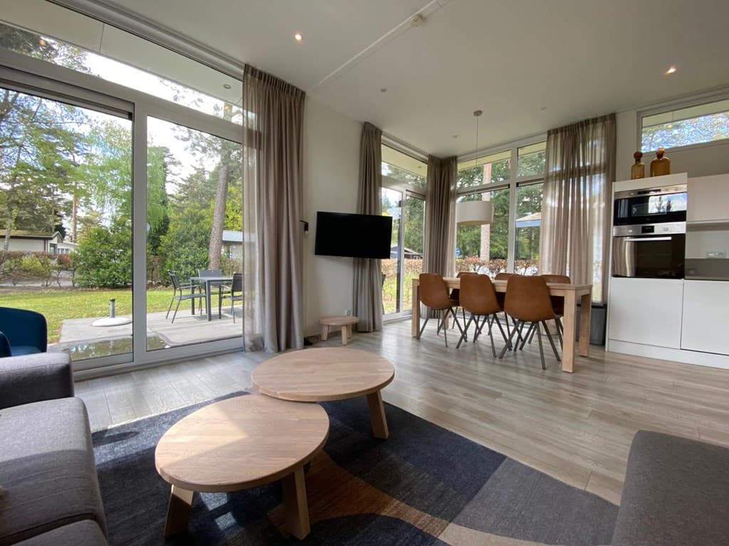 Woonkamer met grote ramen, moderne meubels, eettafel en uitzicht op de tuin en het terras.