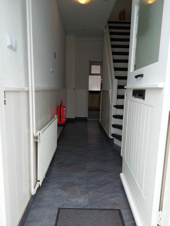 Ingang van de woning met moderne tegels, een trap naar boven en een radiator aan de wand.