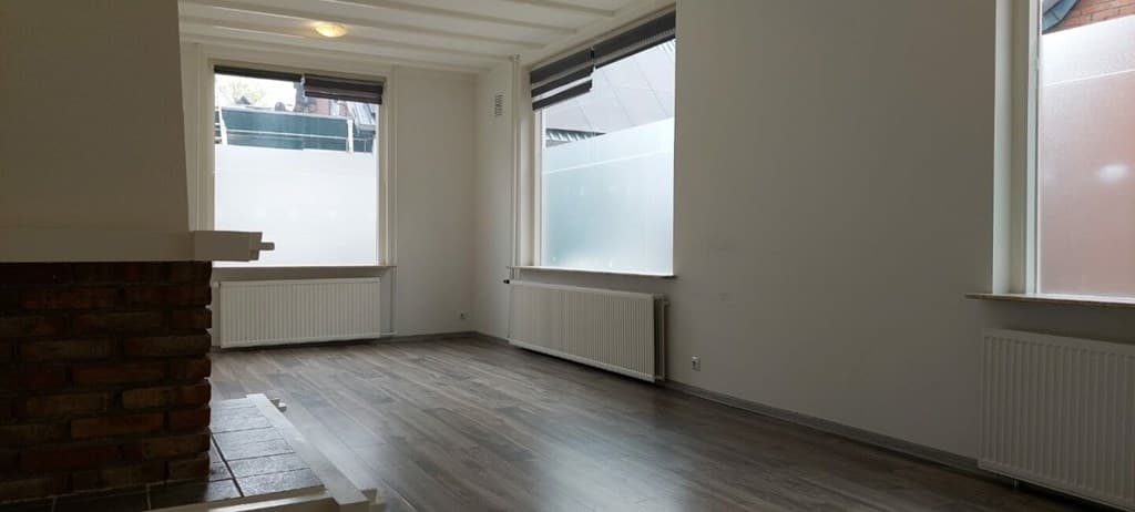 Lichte woonkamer met houten vloer, grote ramen en centrale verwarming, muren in neutrale kleur