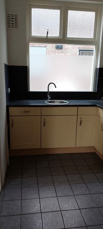 Keuken met lichtgekleurde kastjes, een zwart aanrechtblad en een spoelbak bij een raam met uitzicht naar buiten