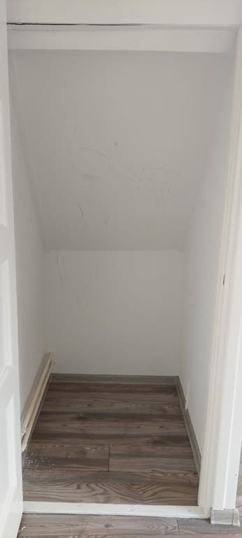 Ingerichte, smalle bergruimte met schuin aflopende wand en houten vloer.