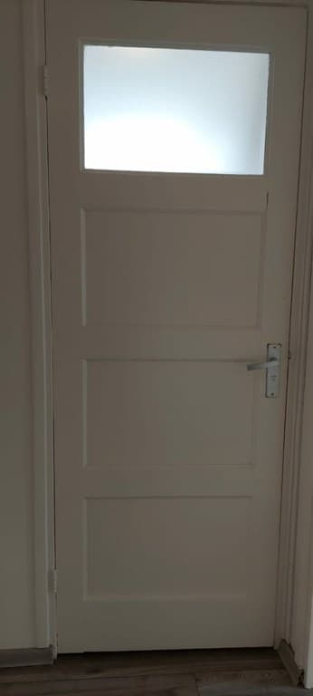 Witte deur met glasruitje in een lichte ruimte met houten vloer en neutrale wanden