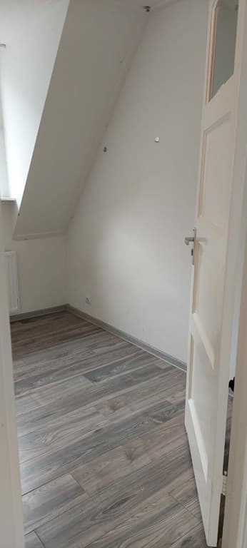 Kamer met schuin plafond, lichte wanden en laminaatvloer, deur naar de gang geopend.