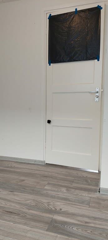 De foto toont een ruimte met een deur bedekt met een zwarte folie en een houten vloer.