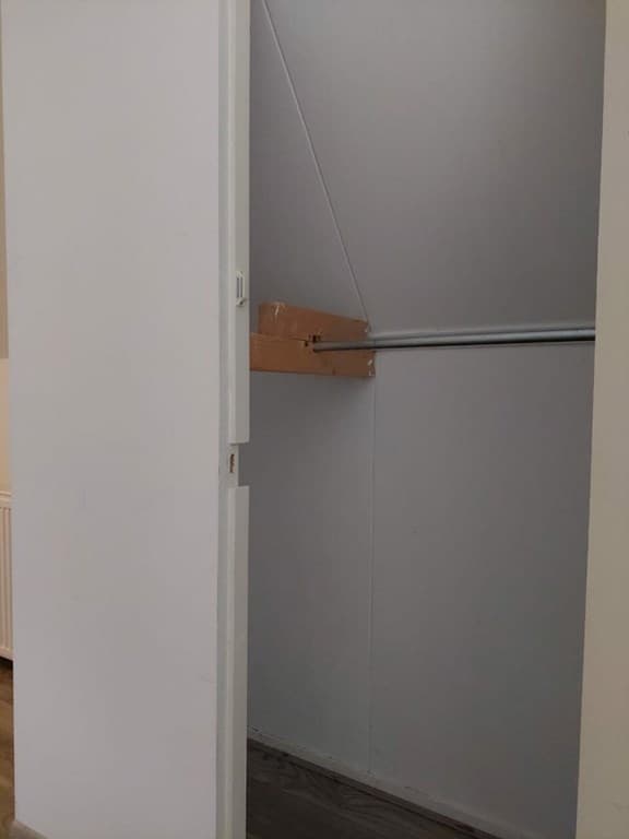 Inbouwkast met een houten balk en een hangroede aan de muur, witte wanden en een houten vloer