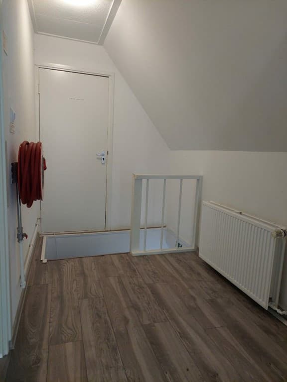 Ruime hal met een deur, verwarming en trap naar beneden, afgewerkt met laminaatvloer en witte wanden