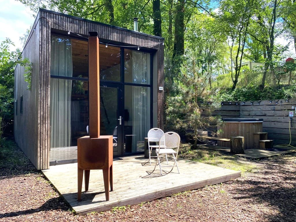 Moderne woning met houten gevel, terras, tuinmeubelen en een houtgestookte kachel, omgeven door bomen.