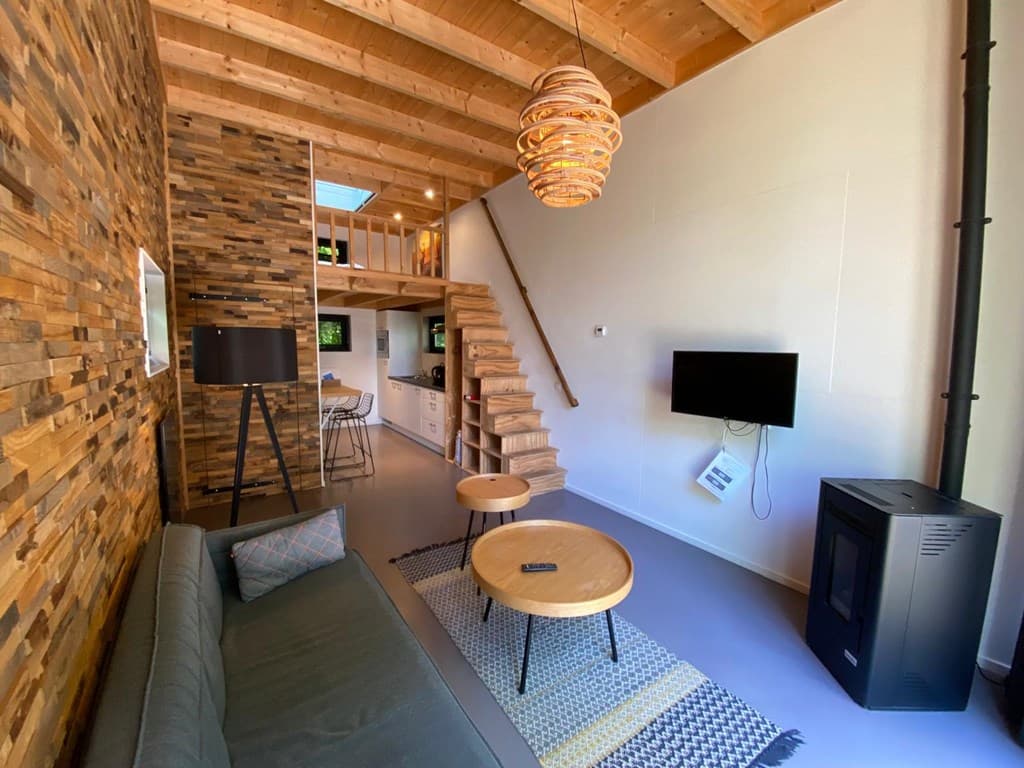 Moderne woonkamer met houten wanden, trap naar boven, zithoek en open keuken met eettafel en barstoelen.