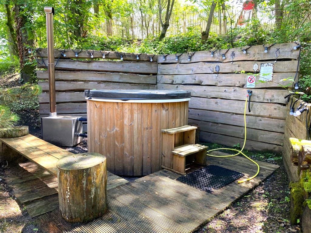 Houten hottub aan een houten wand met traptreden en omringd door groen.