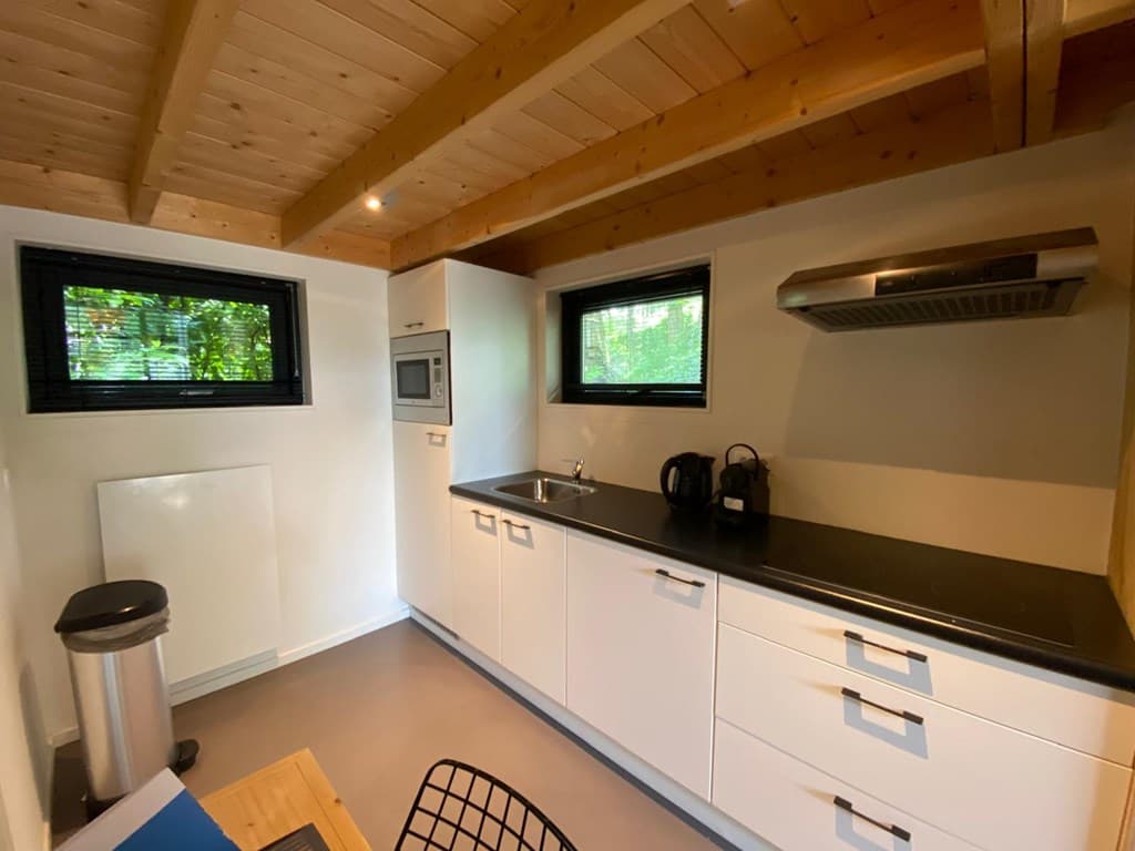 Moderne keuken met witte kasten, inductiekookplaat, oven, koel-vriescombinatie en houten plafond met zichtbare balken