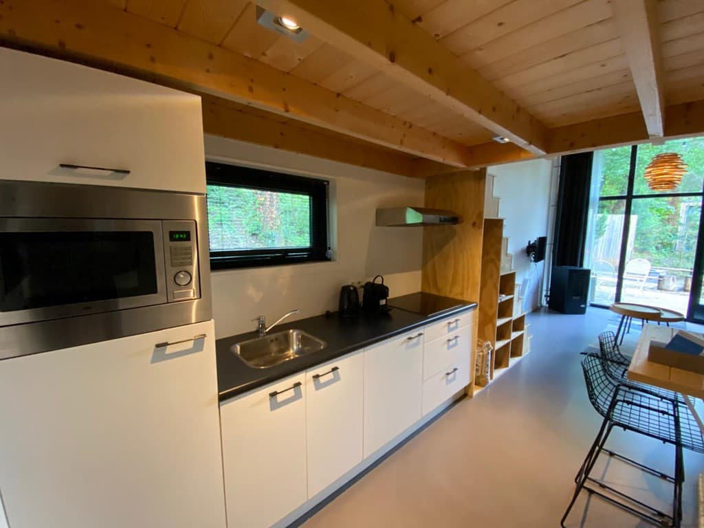 Moderne open keuken met keukenblok, spoelbak, magnetron en eetstoelen met zicht op de tuin door grote ramen