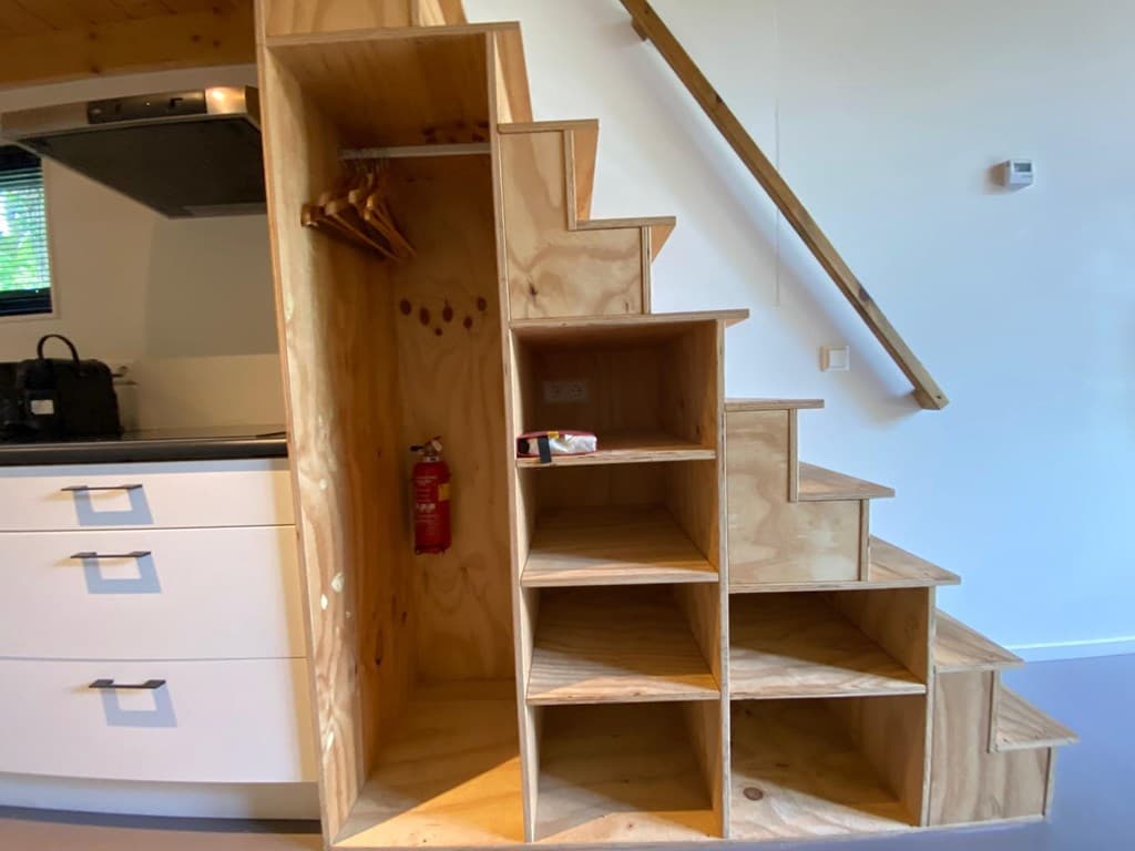 Houten trap met opbergruimte en haakjes in een woning, naast een keukenblok met kasten.
