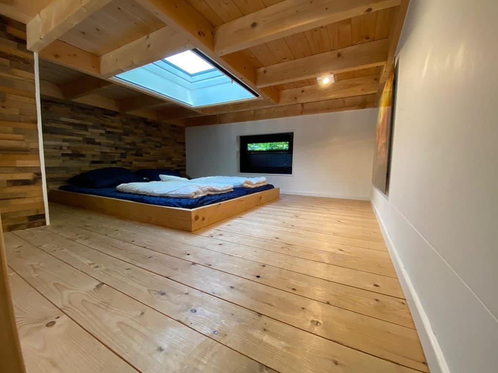 Sfeervolle slaapkamer met houten vloer, plantenwand en dakraam voor natuurlijk licht