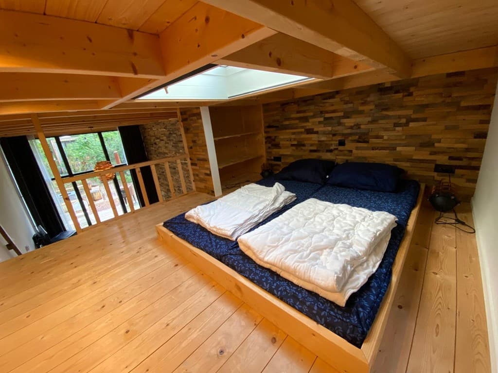 Ruime slaapkamer met houten vloeren en een tweepersoonsbed, bereikbaar via een open trap en met uitzicht op de benedenverdiep