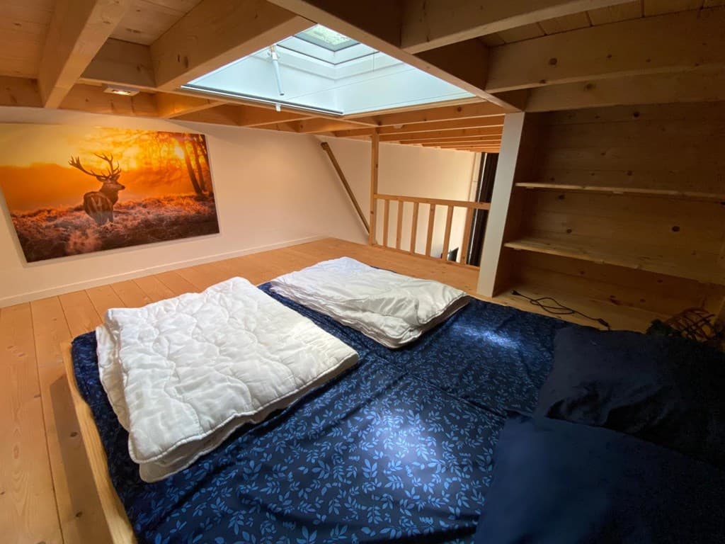 Sfeervolle slaapkamer met houten plafond, dakramen en een bed met dekens en kussens op de vloer