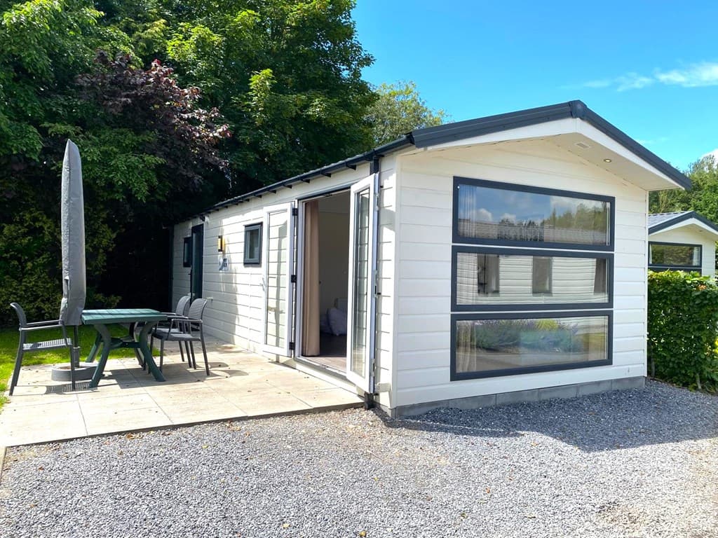 Woning met lichte gevel, grote ramen en een terras met tafel en stoelen, omringd door groen en grindig pad.