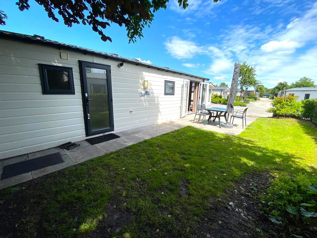 Woning met toegang via een terras, omgeven door gras en bomen, in EuroParcs Zuiderzee.