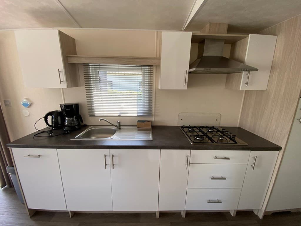 Keuken met modern wit meubilair, spoelbak, kookplaat en koffiezetapparaat in EuroParcs Zuiderzee.