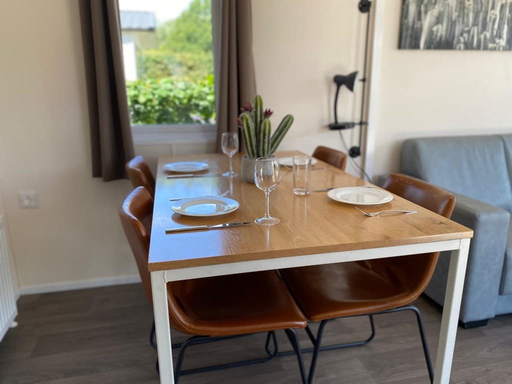Eetkamer met een houten tafel, leren stoelen en glazen, naast een raam met uitzicht op groen.