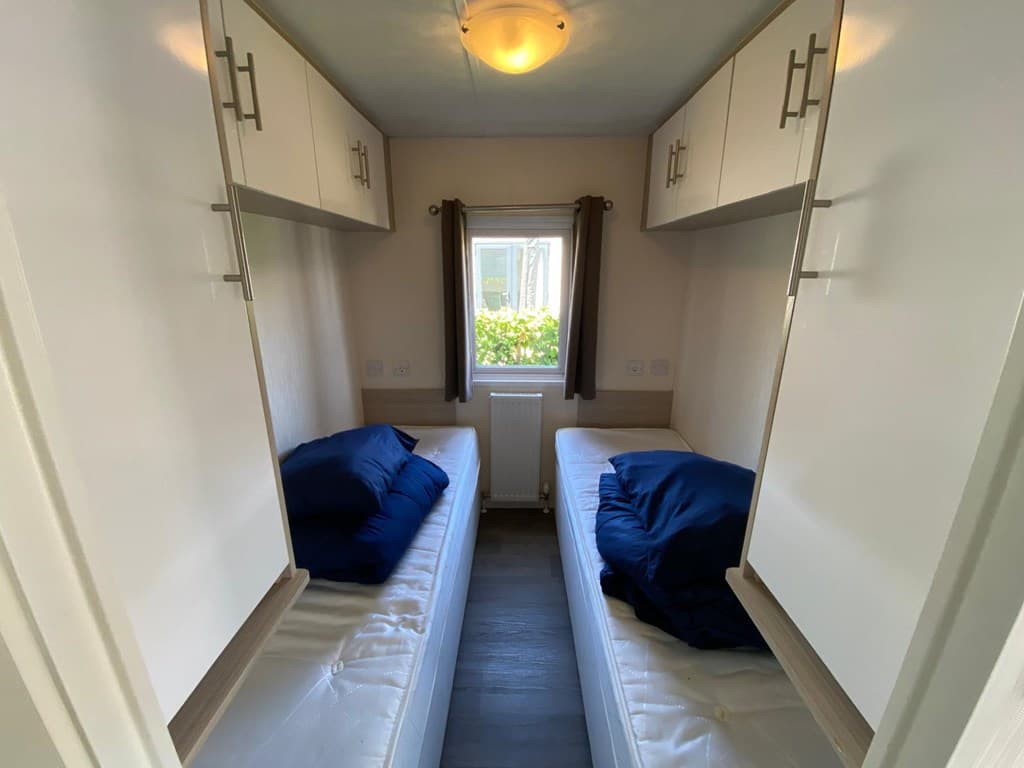 Slaapkamer met twee eenpersoonsbedden en bovenkasten, raam met uitzicht op groene buitenruimte.
