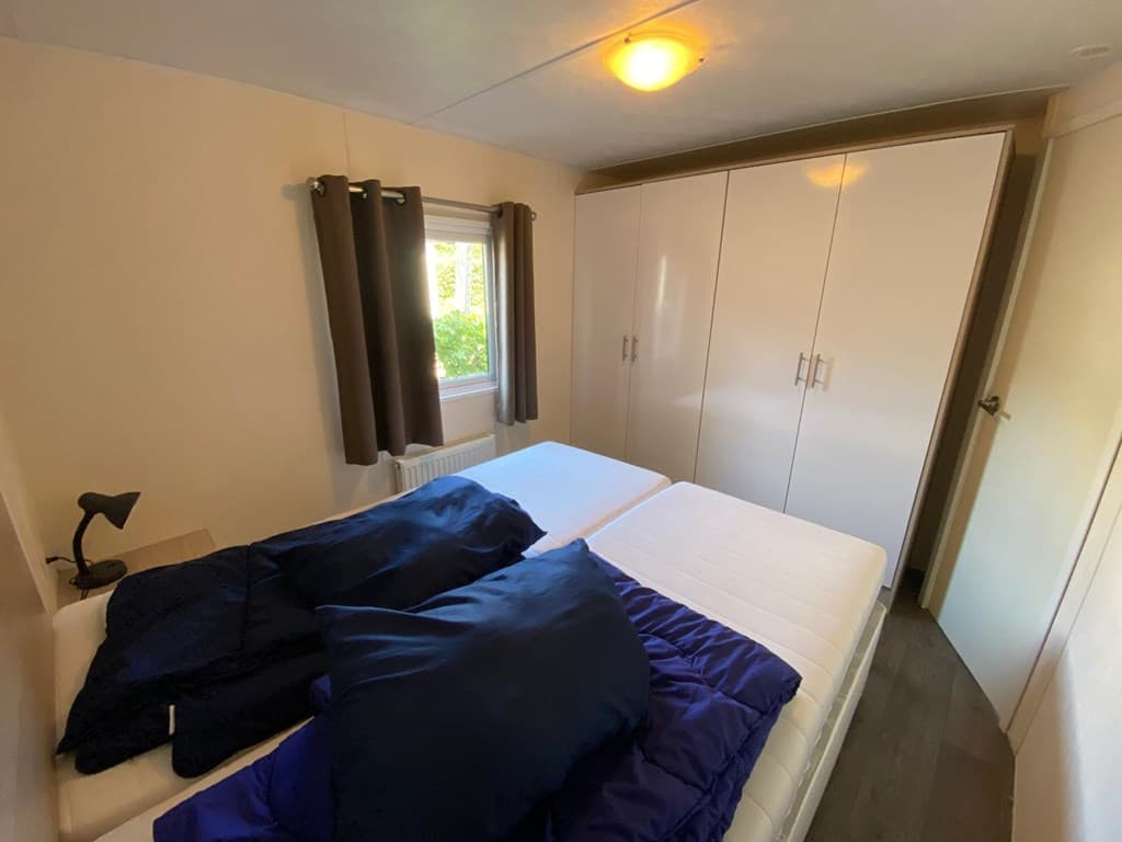 Slaapkamer met twee eenpersoonsbedden, een kledingkast en een raam met uitzicht op de buitenruimte.