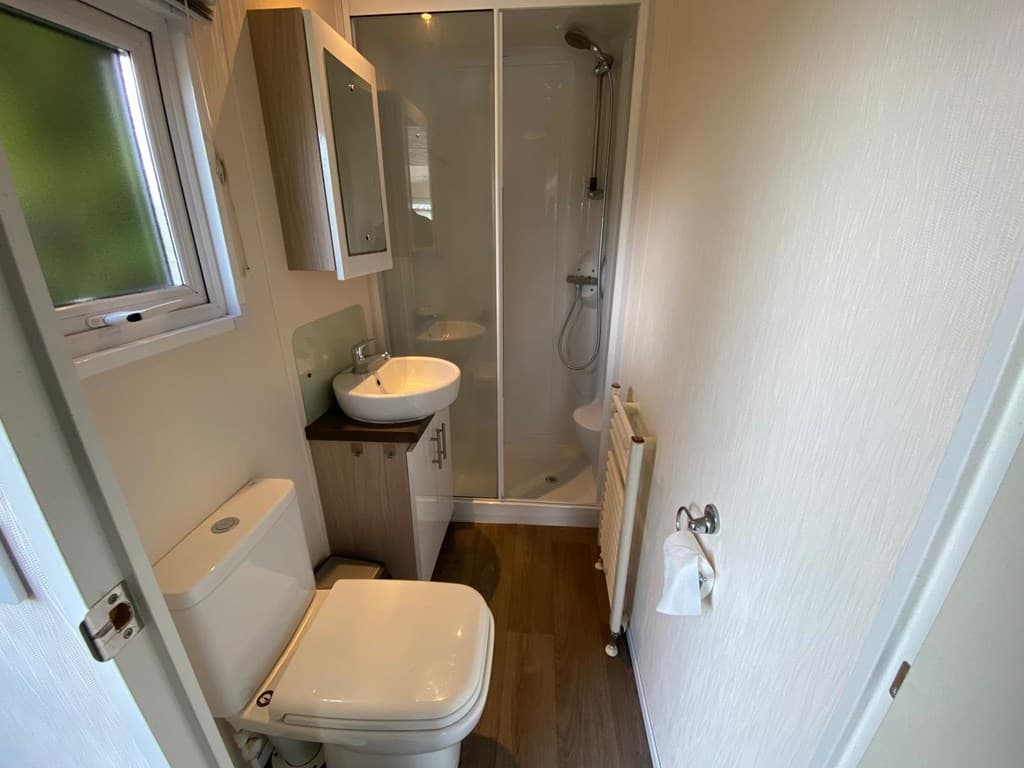 Badkamer met douche, wastafel en toilet in lichte, moderne stijl met houten vloer en raam voor natuurlijk licht