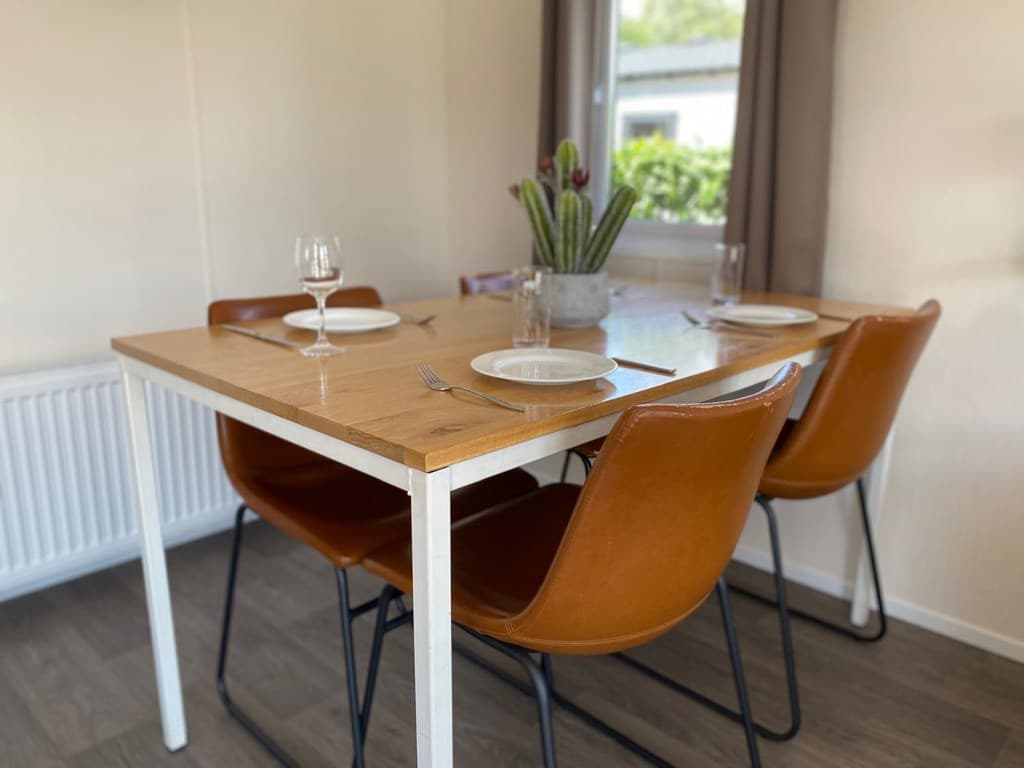 Eetkamertafel met vier leren stoelen, een vaas met planten en servies klaar voor gebruik bij een raam.
