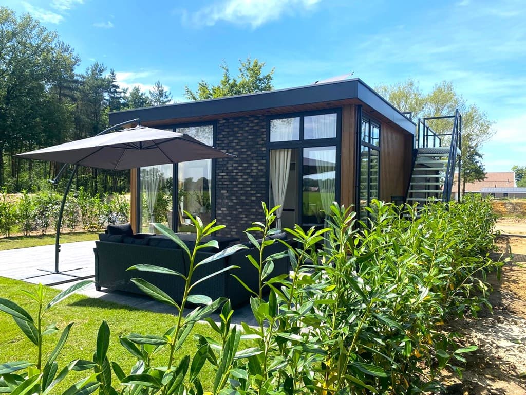 Moderne vakantiewoning met terras, parasol en groene beplanting rondom, gelegen in een bosrijke omgeving