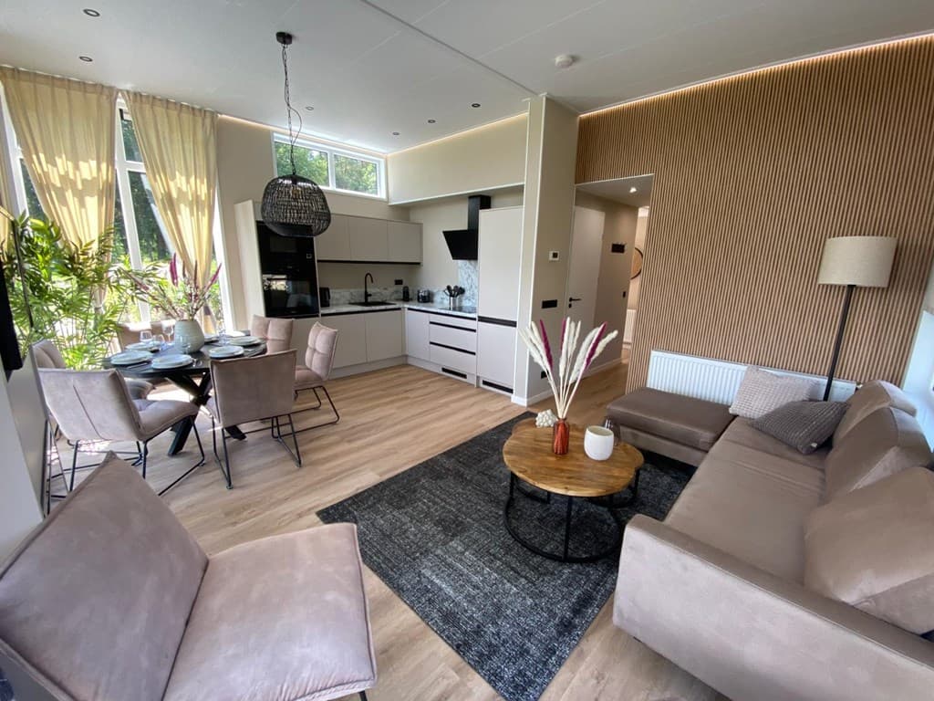 Moderne woonkamer met open keuken, eettafel voor vier, zitbank en decoratieve accessoires in neutrale kleuren.