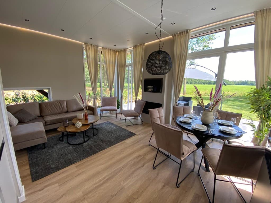 Modern ingerichte woonkamer met bank, eettafel en uitzicht op een groene omgeving vanuit grote ramen