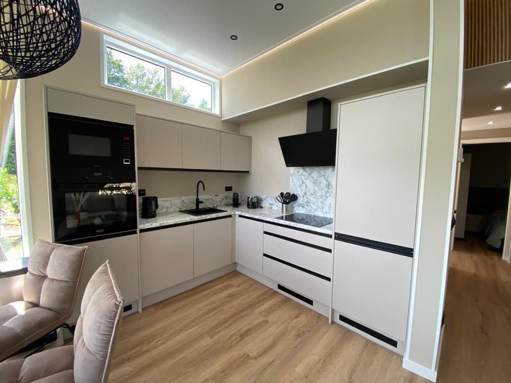 Moderne keuken met lichte kastjes, marmeren werkblad en zwarte accenten, naast een eettafel met comfortabele stoelen