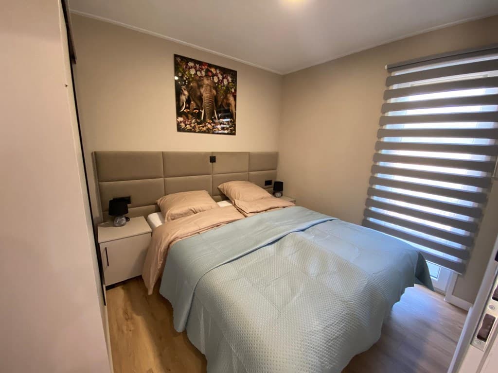 Slaapkamer met tweepersoonsbed, nachtkastjes en een groot raam met jaloezieën. Decoratie met een olifantenfoto aan de muur.