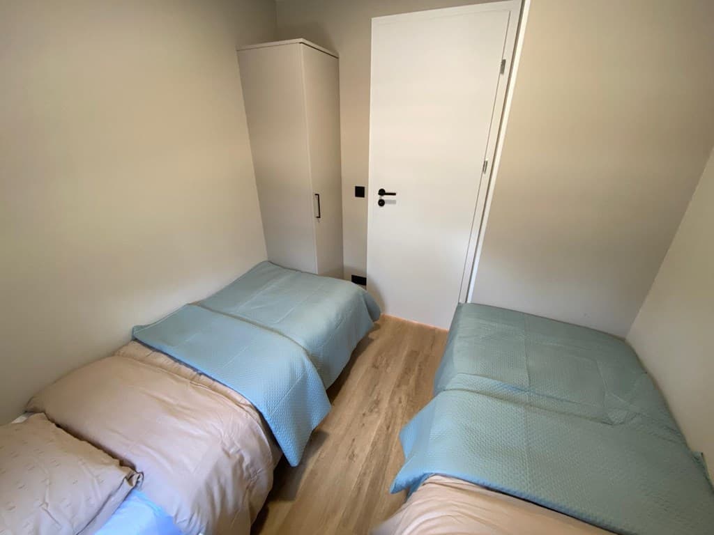 Slaapkamer met twee aparte bedden, een kledingkast en een deur naar de gang.