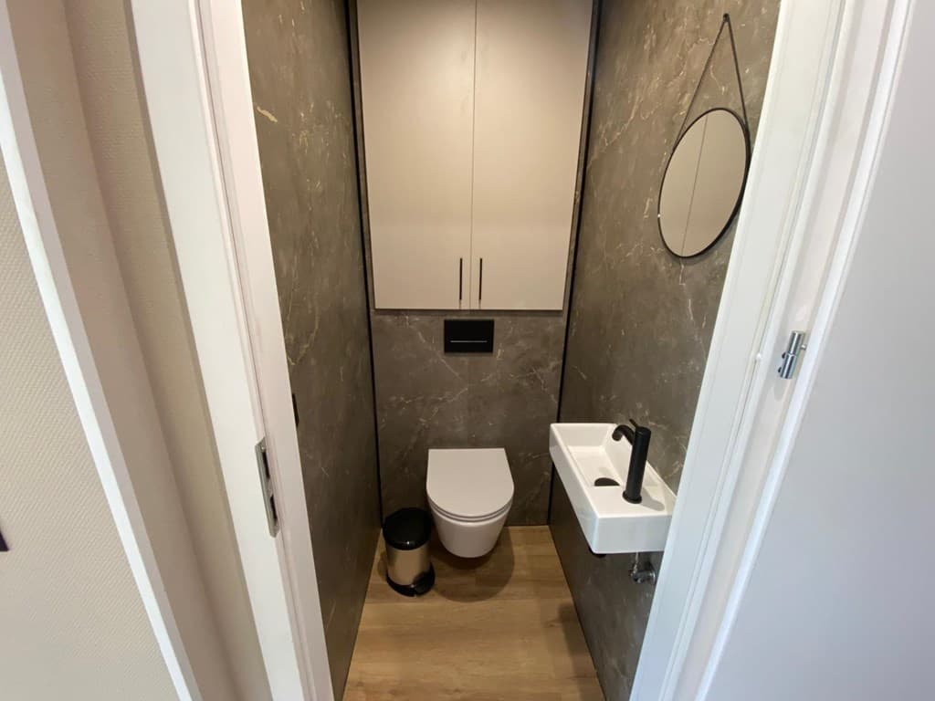 Toilet met moderne afwerking, een wandcloset, wastafel en een ronde spiegel op de muur.